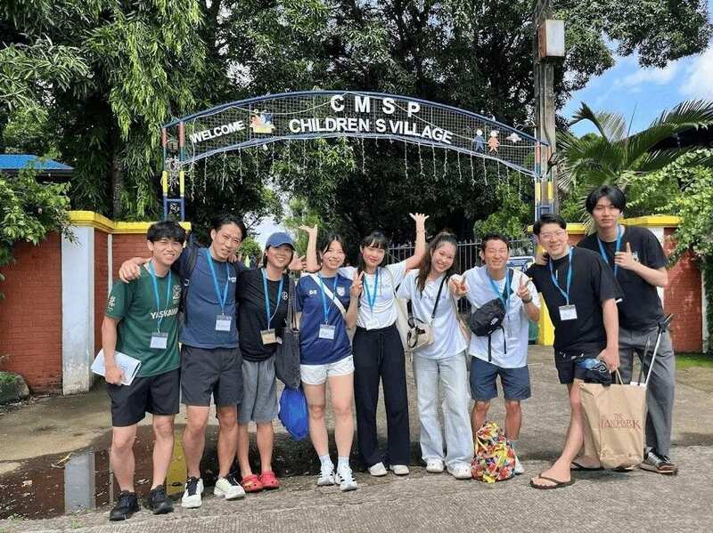 Maho, Reeracoen Malaysia Career Advisor, posing with team members outside the entrance sign of CMSP Children's Village