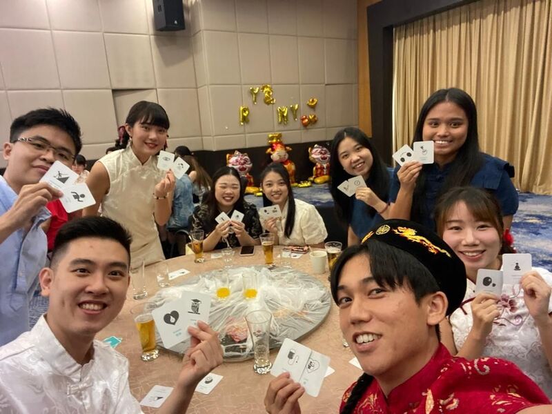 Maho, Reeracoen Malaysia Career Advisor, holding game cards with colleagues around a dinner table at a company event.